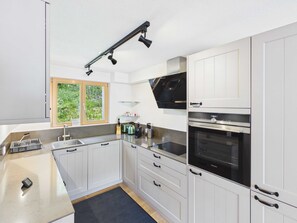 Una cocina moderna con armarios blancos, horno empotrado y ventana con vista a la vegetación.
