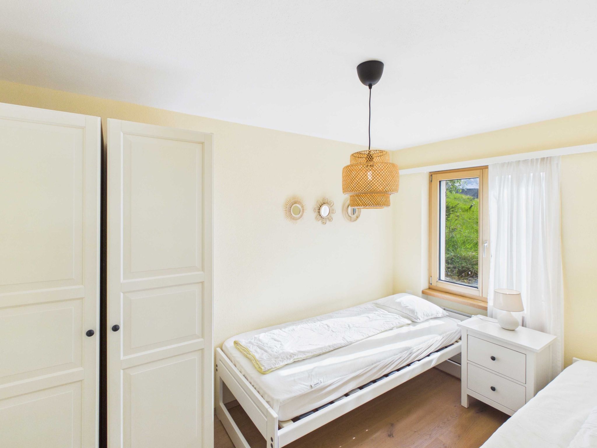 Un dormitorio con cama, mesita de noche, ventana con cortinas y armario.