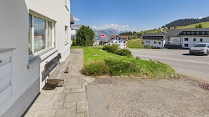 Edificio con ingresso lastricato, una panchina e vista su una strada con un'auto.