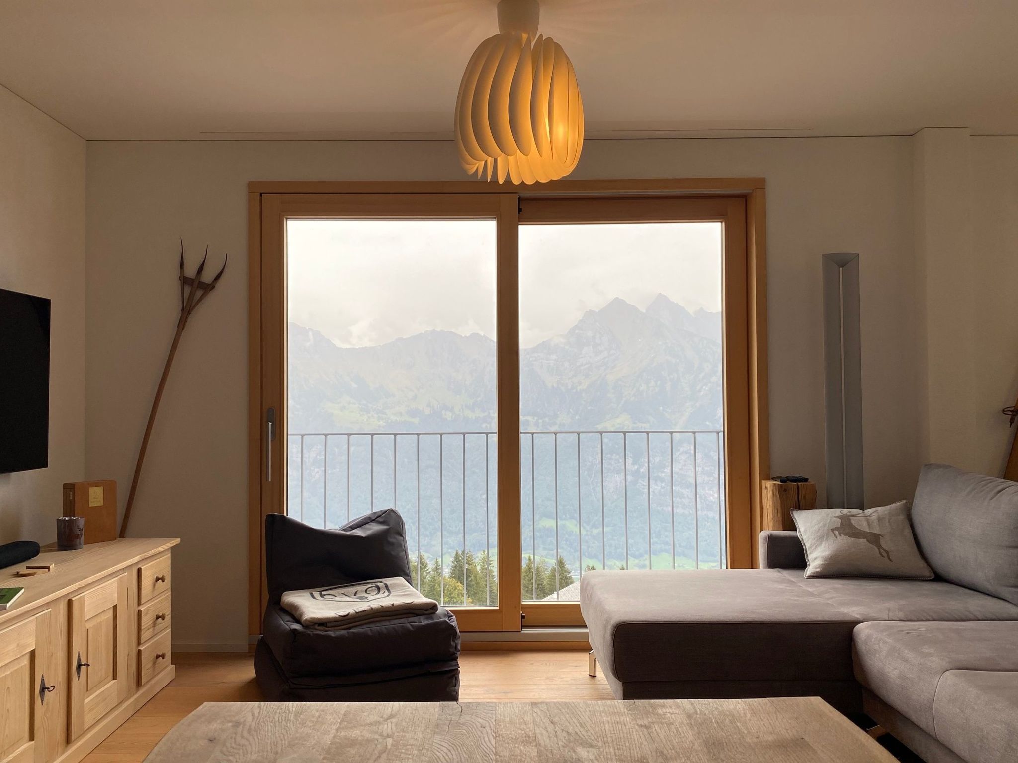 A modern living room with a large sliding glass door leading to a balcony with a mountain view.