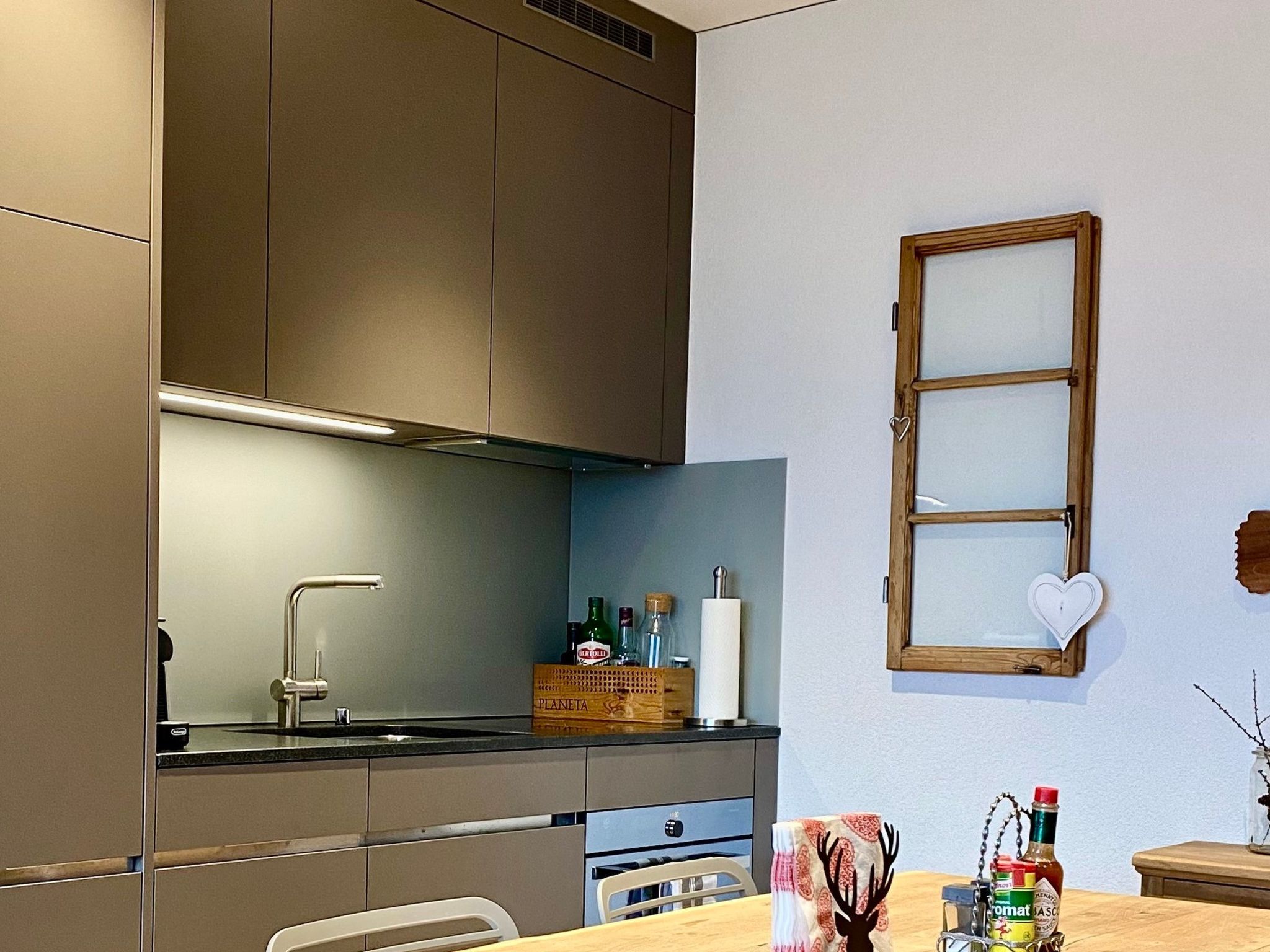 A modern kitchen with a built-in oven, a sink, and a window with a heart-shaped decoration.