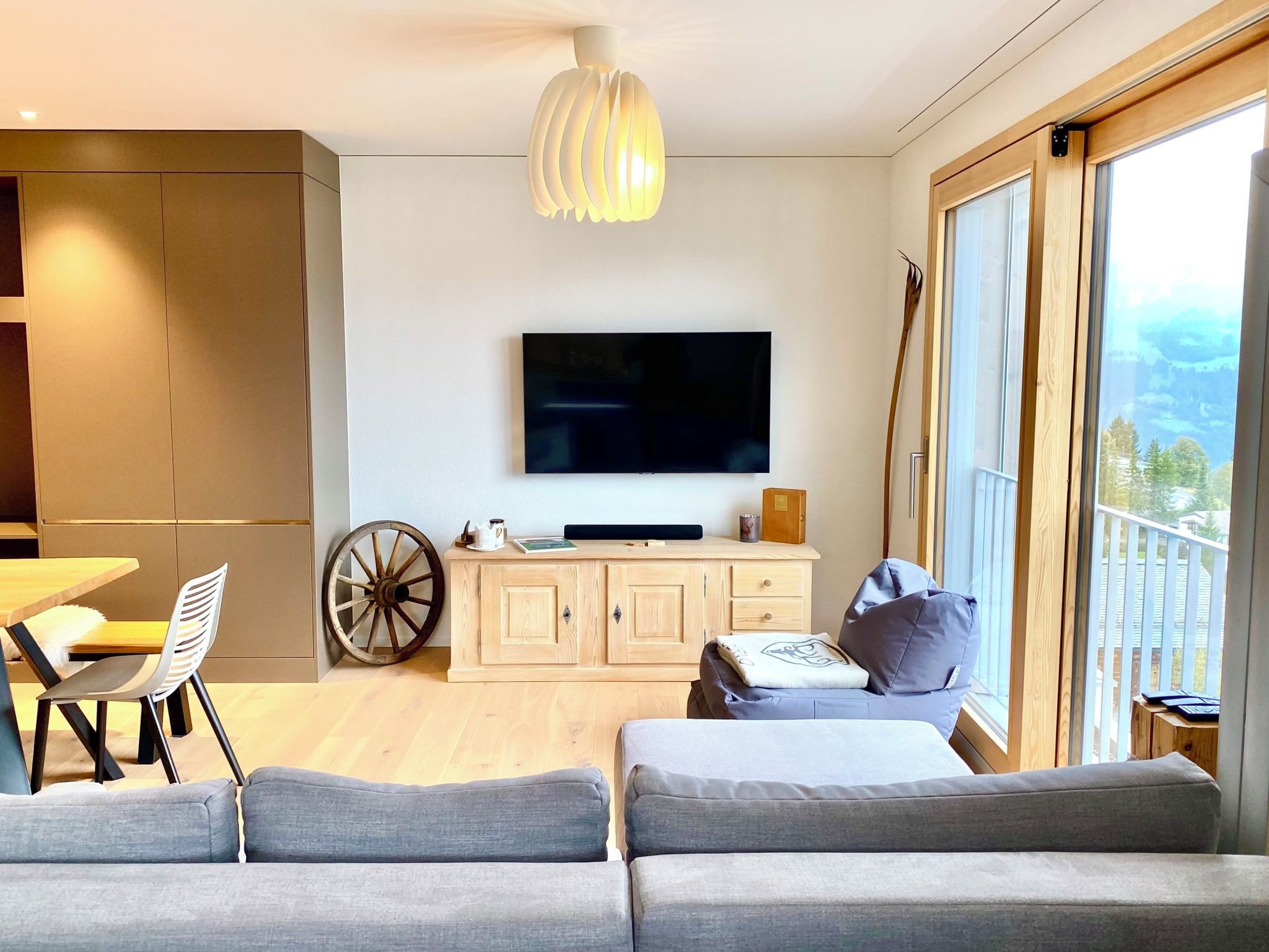 Een moderne woonkamer met een flatscreen televisie, een bank, een eethoek met een houten tafel en stoelen, en een groot raam met uitzicht.