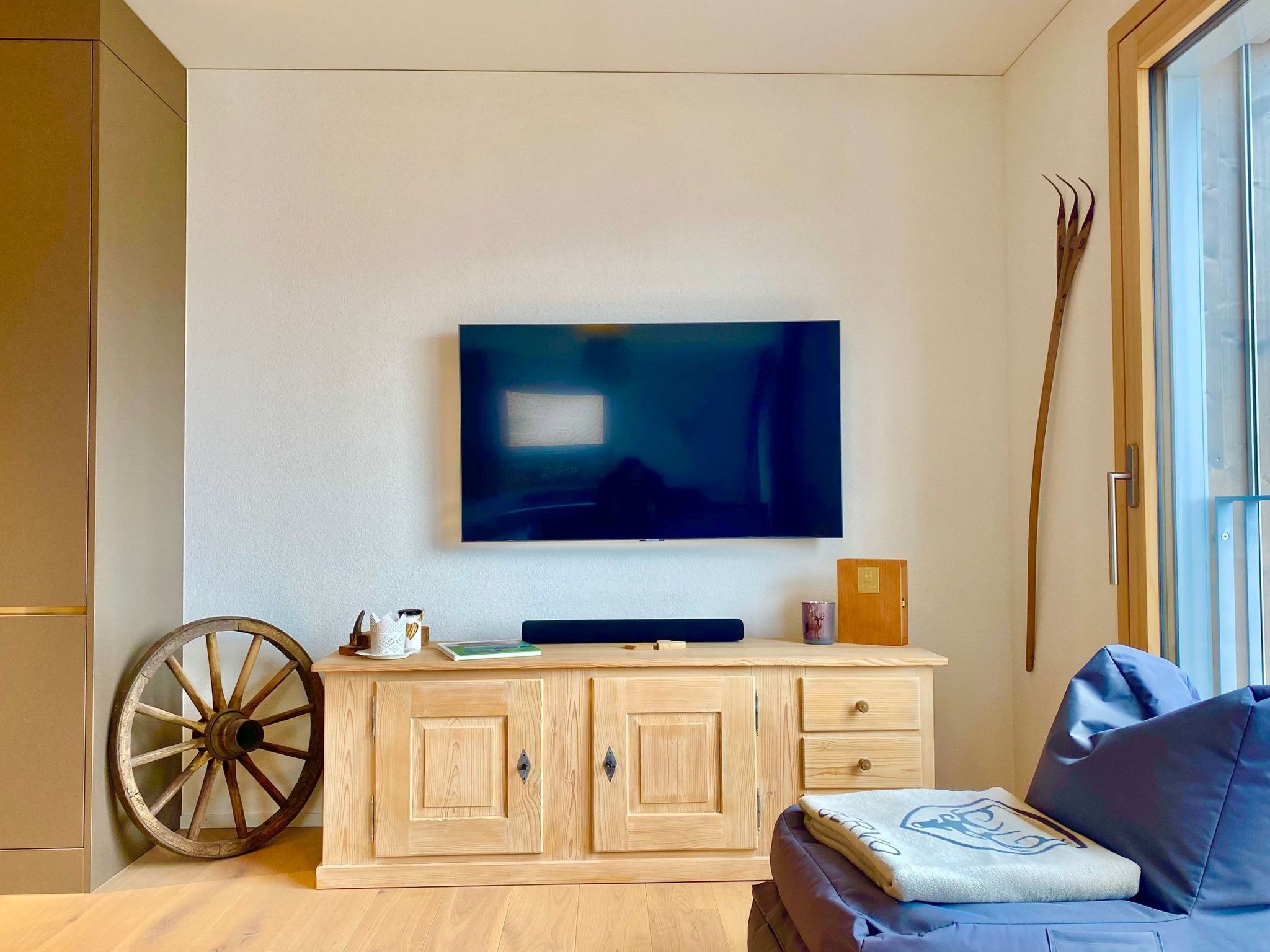 Una sala moderna con una televisión de pantalla plana montada en la pared, un mueble de madera con cajones, una rueda de madera grande y un sofá azul.