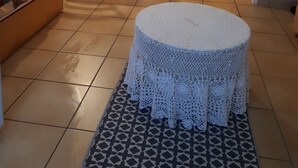 Uma sala de estar com sofá, uma mesa de jantar com cadeiras, uma porta branca e uma área de cozinha com azulejos na parede.