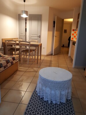Ein Wohnzimmer mit einer Couch, einem Esstisch mit Stühlen, einer weißen Tür und einer Küchenzeile mit Fliesenrückwand.