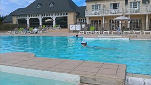 Ein Schwimmbecken mit Liegestühlen und ein Gebäude mit Balkonen im Hintergrund.