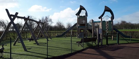Een speeltuin met schommels en glijbanen, omringd door een hek.
