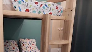 Uma cama beliche com escada, uma cama de solteiro com edredom colorido com tema espacial, e um radiador branco.