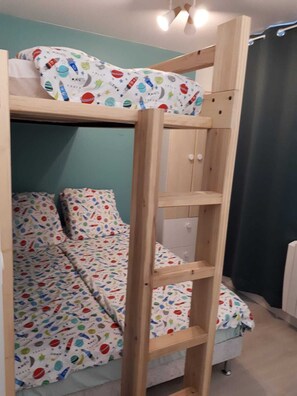 Ein Etagenbett mit einer Leiter, ein Einzelbett mit einer farbenfrohen Bettdecke zum Thema Weltraum und eine weiße Heizung.