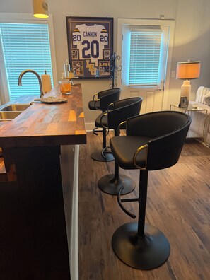 Una cocina con encimera de madera, un lavamanos y tres taburetes negros.