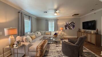 A living room with a sectional sofa, a glass coffee table, a gray armchair, a patterned rug, and a flat-screen TV.