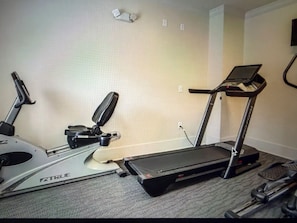A treadmill and elliptical machine in a room with carpet flooring and a plain wall. - Tiger Condo at LSU!  Walk to Tiger Stadium & PMAC! (Baton Rouge)