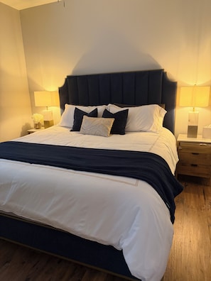 A neatly made bed with a dark headboard, white bedding, and a bedside table with a lamp.