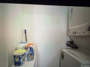 A laundry area with a washing machine, detergent bottles, and a mop. - Tiger Condo at LSU!  Walk to Tiger Stadium & PMAC! (Baton Rouge)