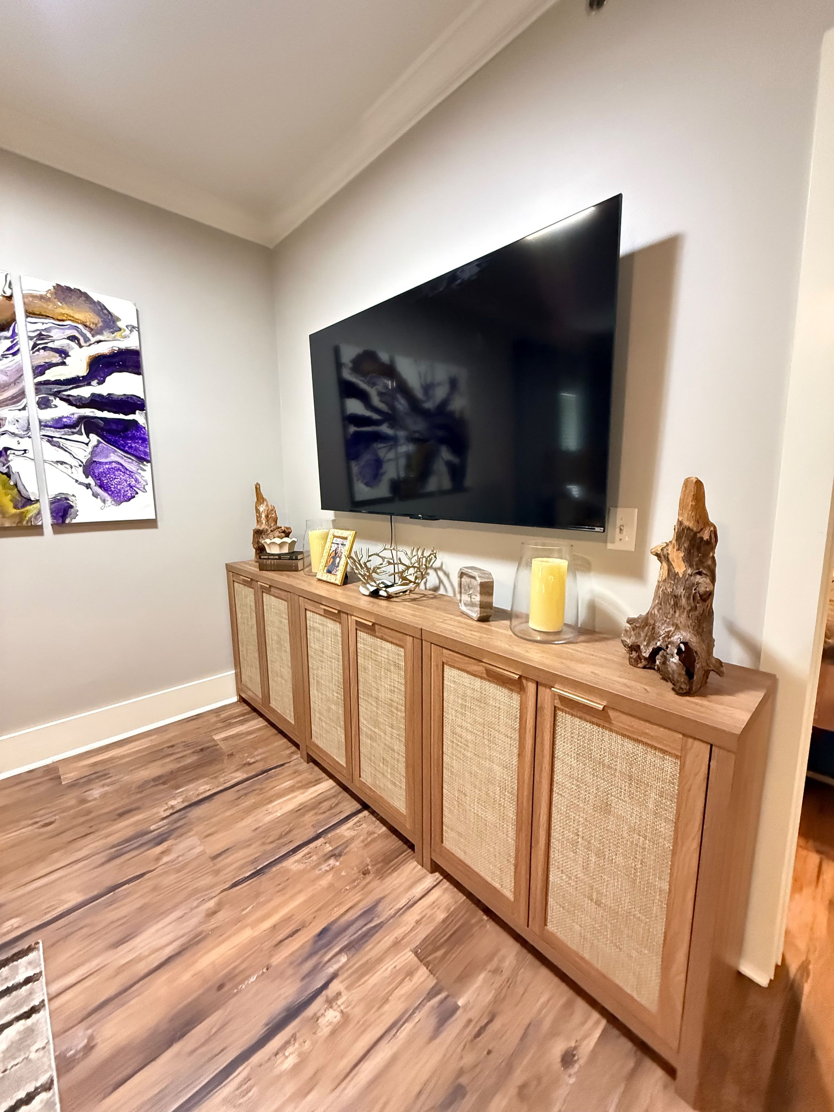 A modern living room with a flat-screen TV mounted on a wall, a wooden console table with decorative items, and a wooden floor.