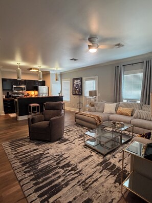 A living room with a sofa, armchair, and coffee table, a kitchen with appliances, and a dining area.