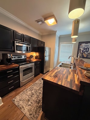 A modern kitchen with dark cabinetry, stainless steel appliances, and a wooden island.