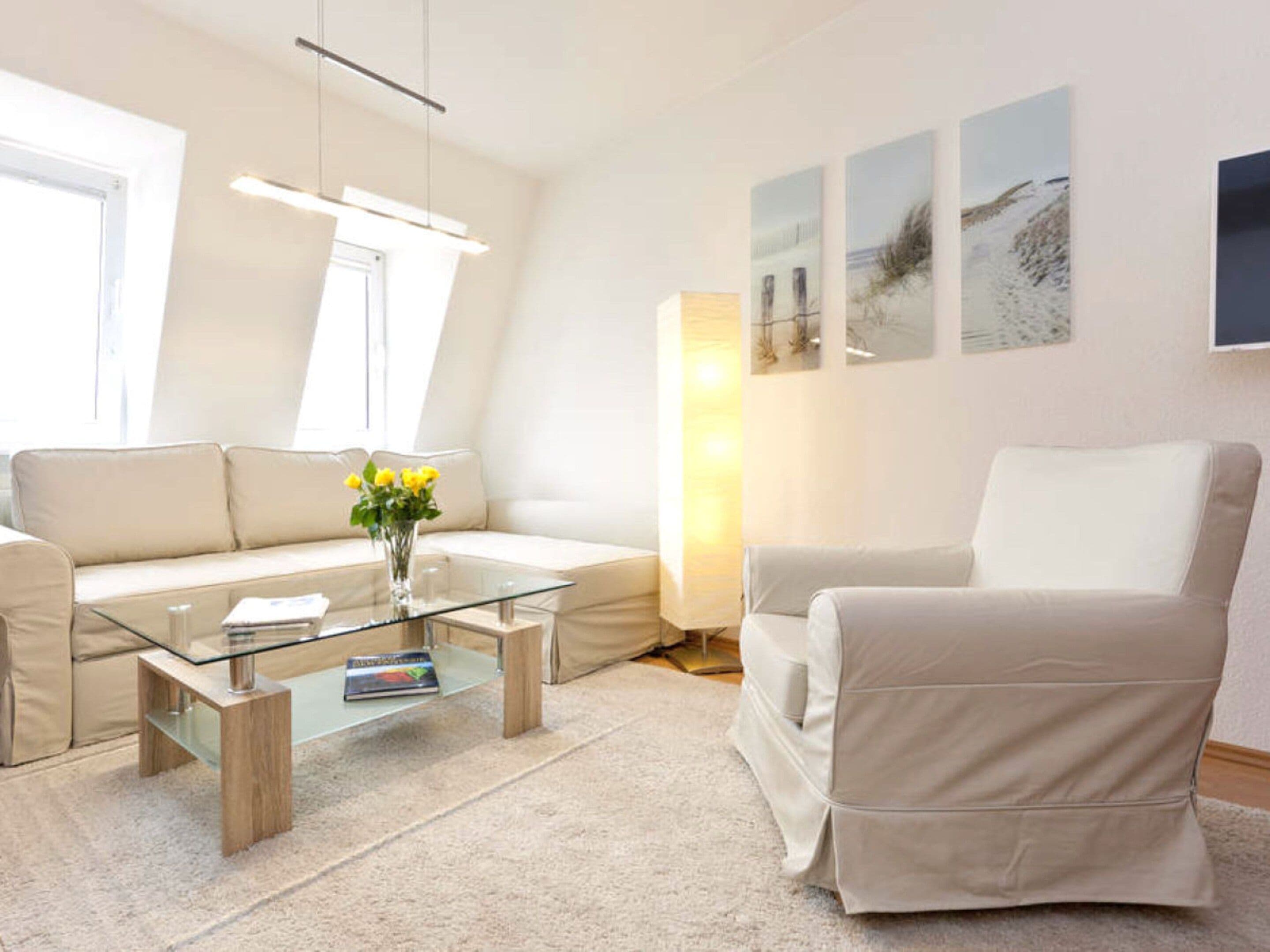 En moderne stue med et glasbord, beige sofaer og en hvid lænestol.
