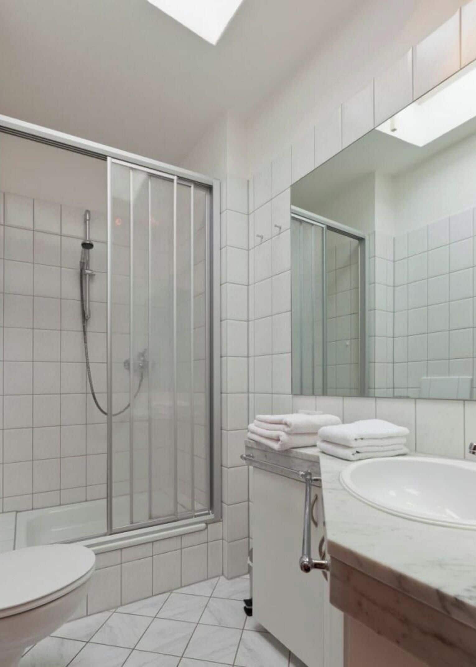 Une salle de bain moderne avec une douche à parois de verre, un lavabo blanc et un grand miroir.