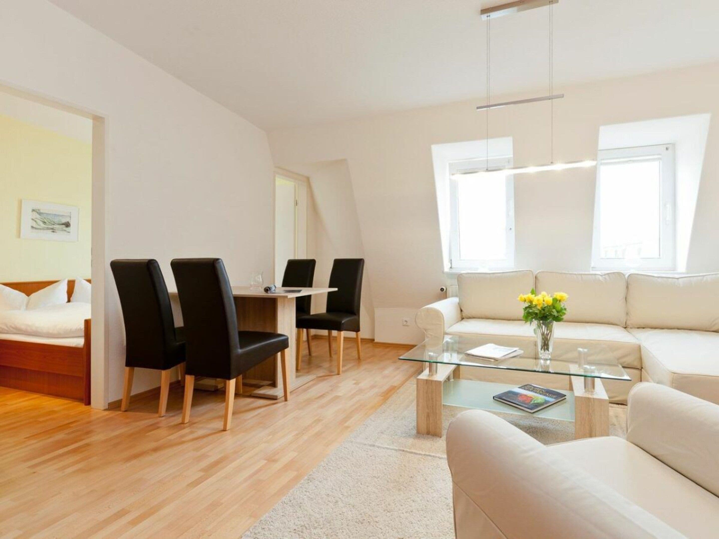 Ein modernes Hotelzimmer mit einem Bett, einem Essbereich mit Stühlen, einem Sofa und einem Glastisch.