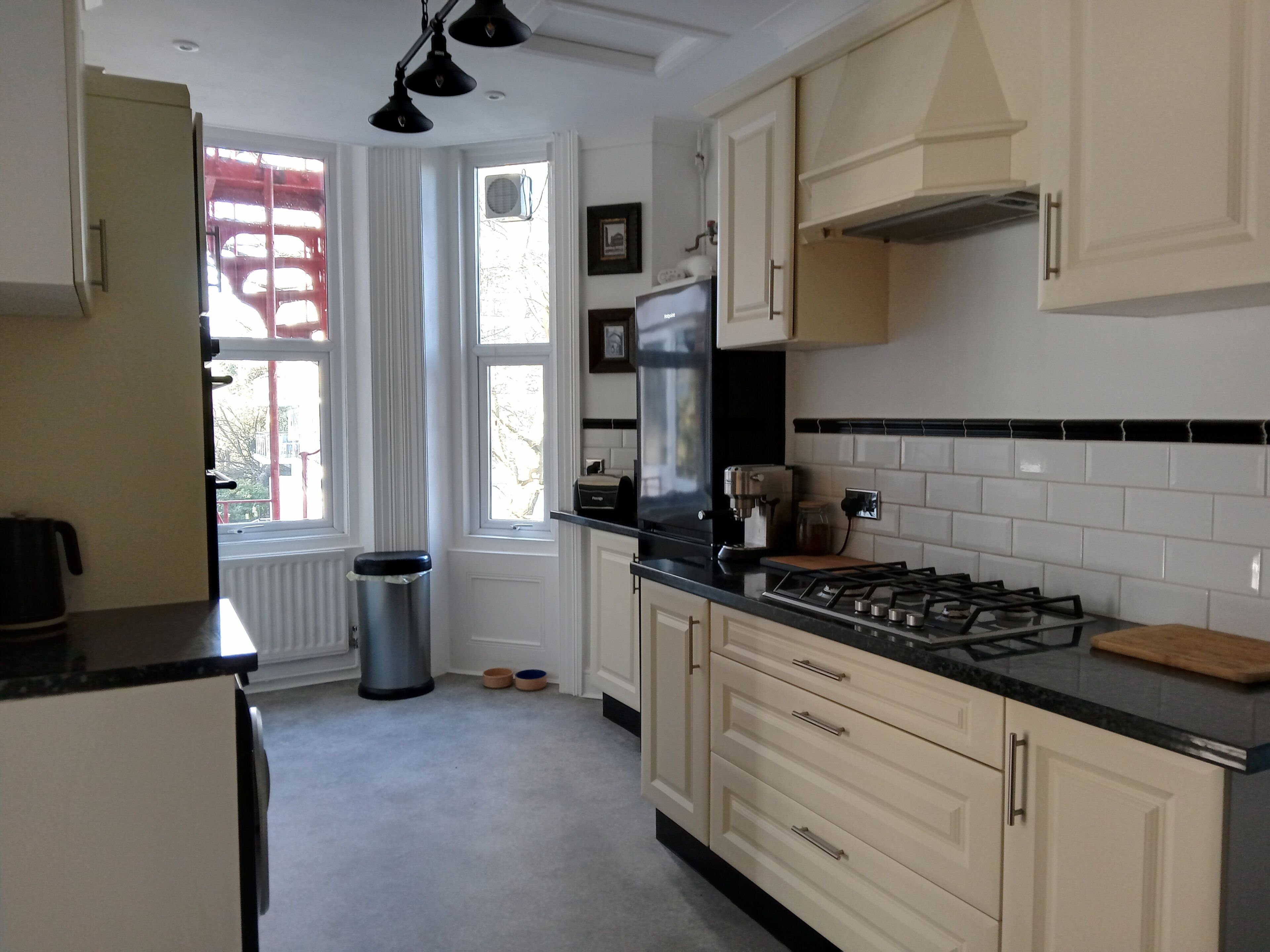 A kitchen with a gas stove, a trash can, and a window with a view of trees.