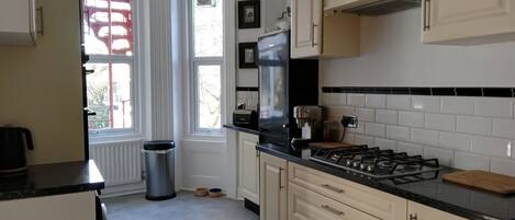 A kitchen with a gas stove, a trash can, and a window with a view of trees.