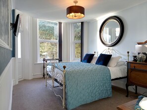 A bedroom with a bed, a dresser, a mirror, and a window with a view of trees. - Luxury Beachfront Apartment in Bournemouth (Bournemouth)