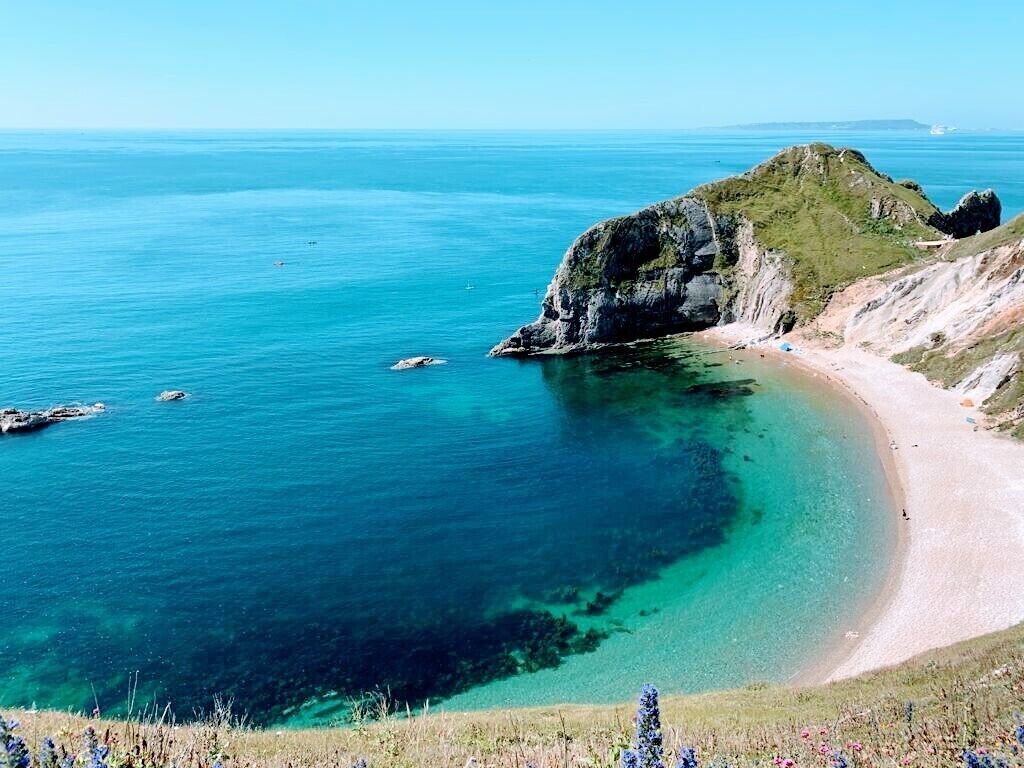 Un paisaje costero con una playa despejada, afloramientos rocosos y una colina cubierta de hierba.