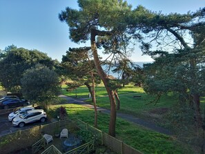 A view of a parking area with cars, a grassy field, and a pathway leading to a bench. - Luxury Beachfront Apartment in Bournemouth (Bournemouth)