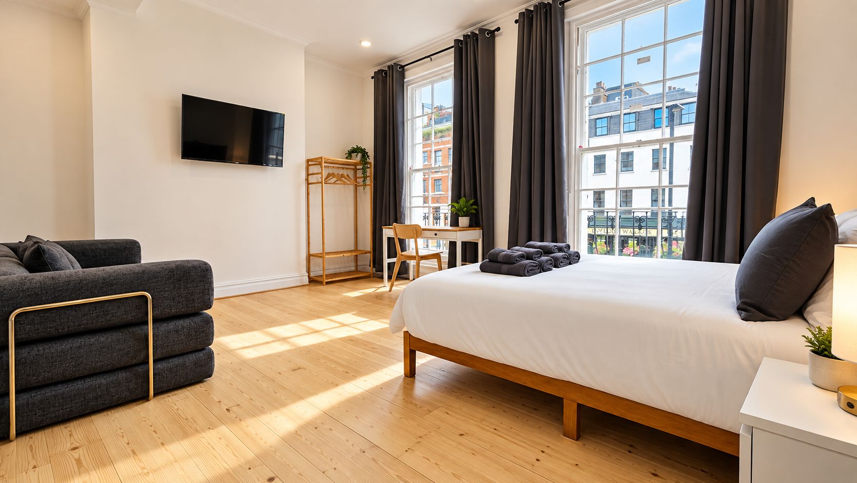 Una habitación de hotel con cama, sofá, televisor, escritorio y ventana con cortinas.