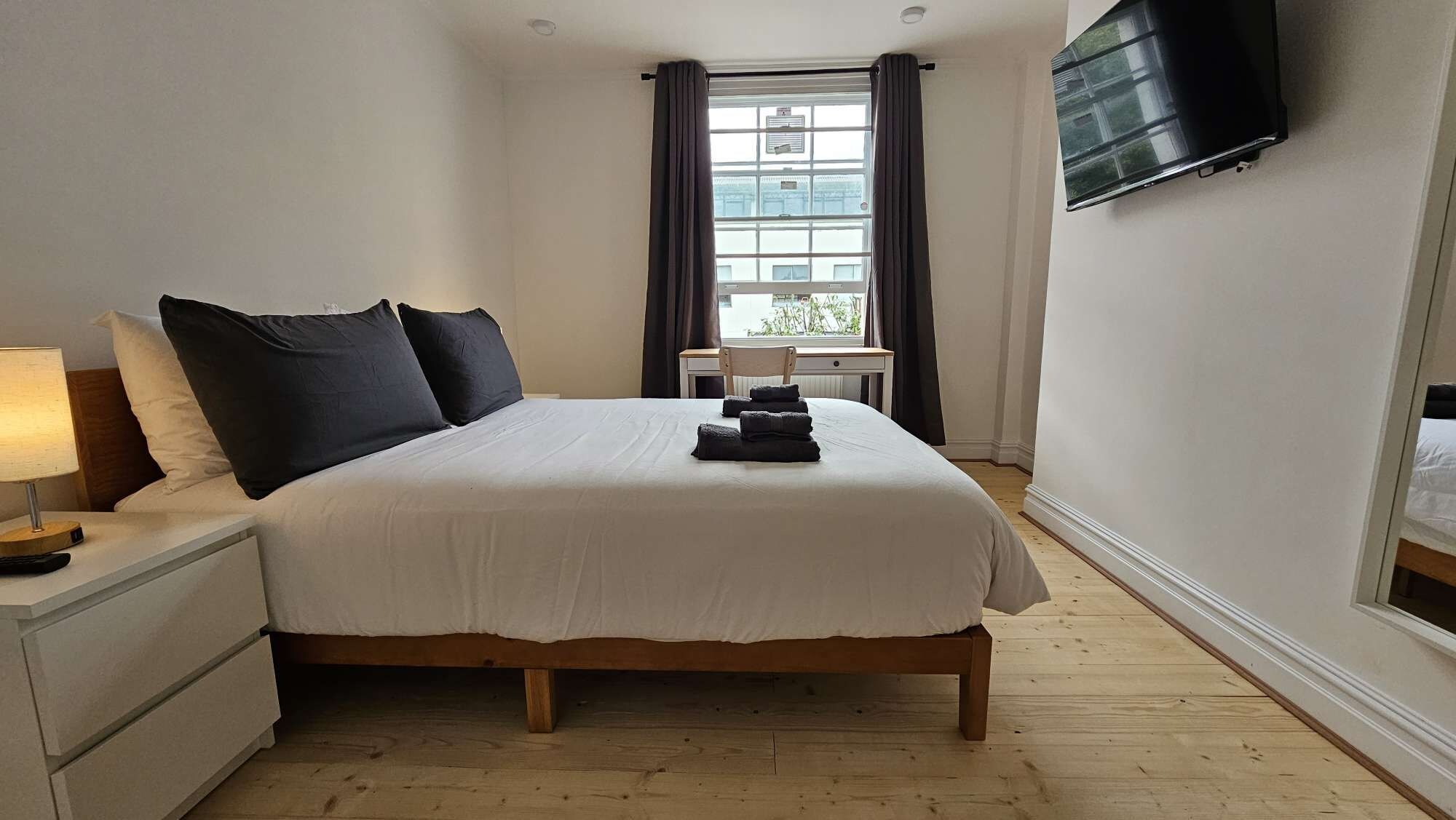 Una habitación de hotel con cama, escritorio, televisión y ventana con cortinas.