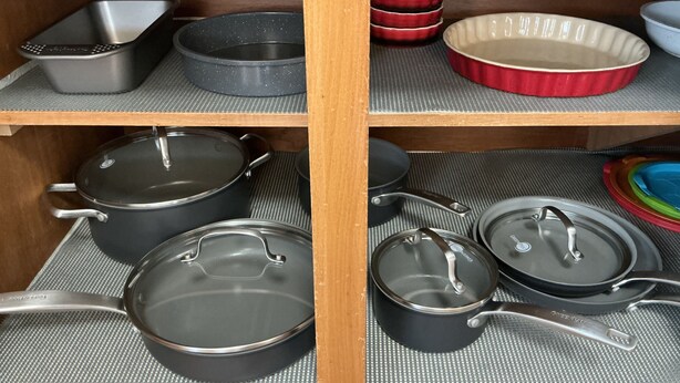 Uma prateleira na cozinha com diversos utensílios de cozinha, incluindo panelas, frigideiras e assadeiras.