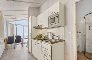 A modern kitchen with a microwave, sink, and cabinets. There is a dining area with chairs and a table. - Holiday Home With 1 Bedroom (Braunlage)