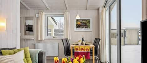 Una sala de estar moderna con un sofá, una mesa de comedor con sillas, un radiador, una ventana con cortinas y vistas al exterior.