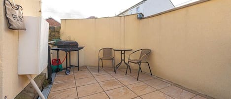 Un patio con una parrilla, dos sillas y una mesa.