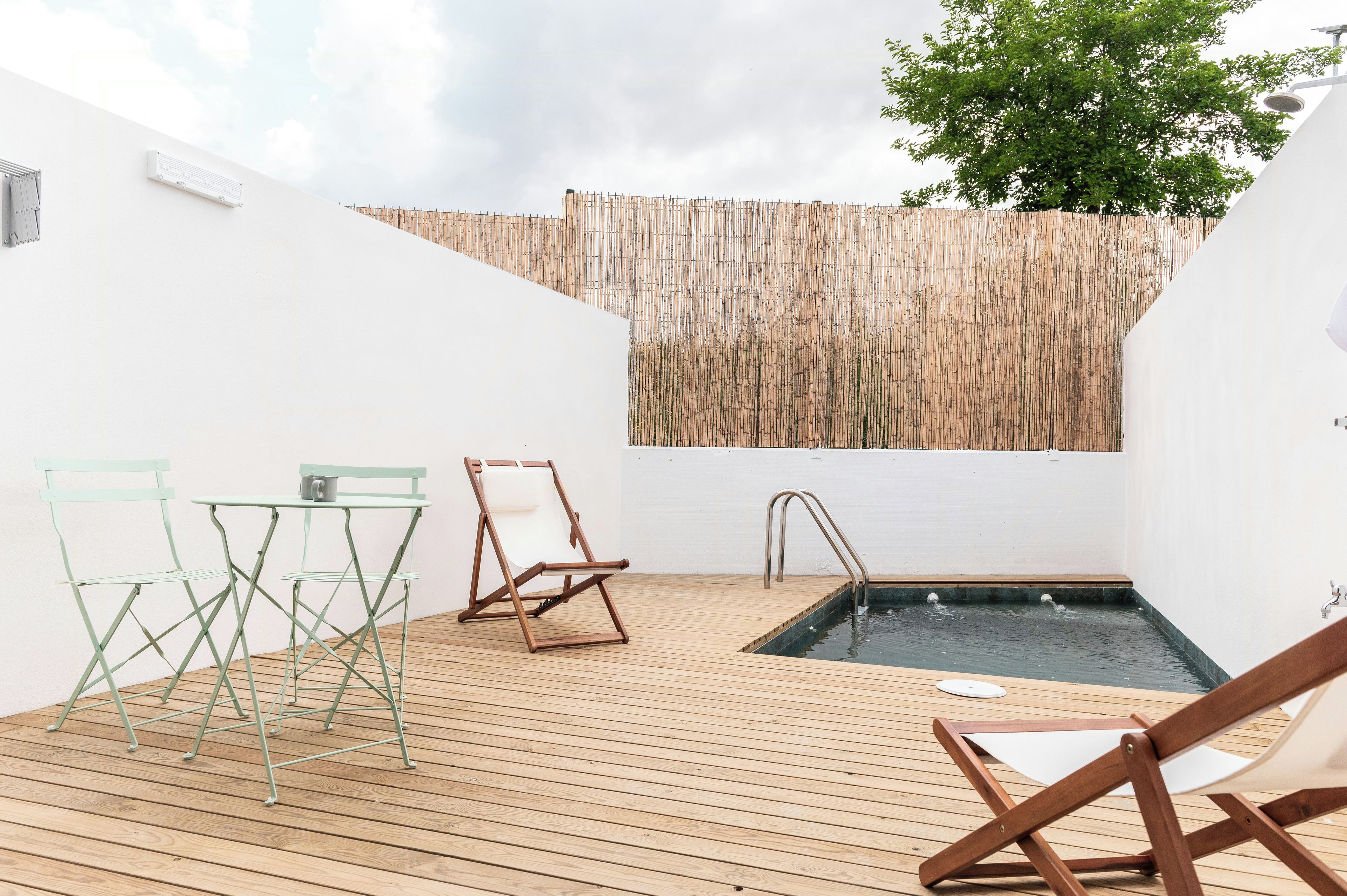 Una terraza de madera con piscina, dos sillas y una pared de bambú.