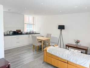 A modern, well-lit room with a bed, a dining table with chairs, a kitchen area with a window, and a floor lamp. - well furnished flat at city center (Kingston upon Hull)