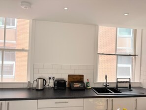 A kitchen with white cabinets, a black countertop, a toaster, a kettle, and a bread box. - well furnished flat at city center (Kingston upon Hull)