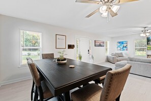 A modern dining area with a dark wooden table, cushioned chairs, and a ceiling fan.