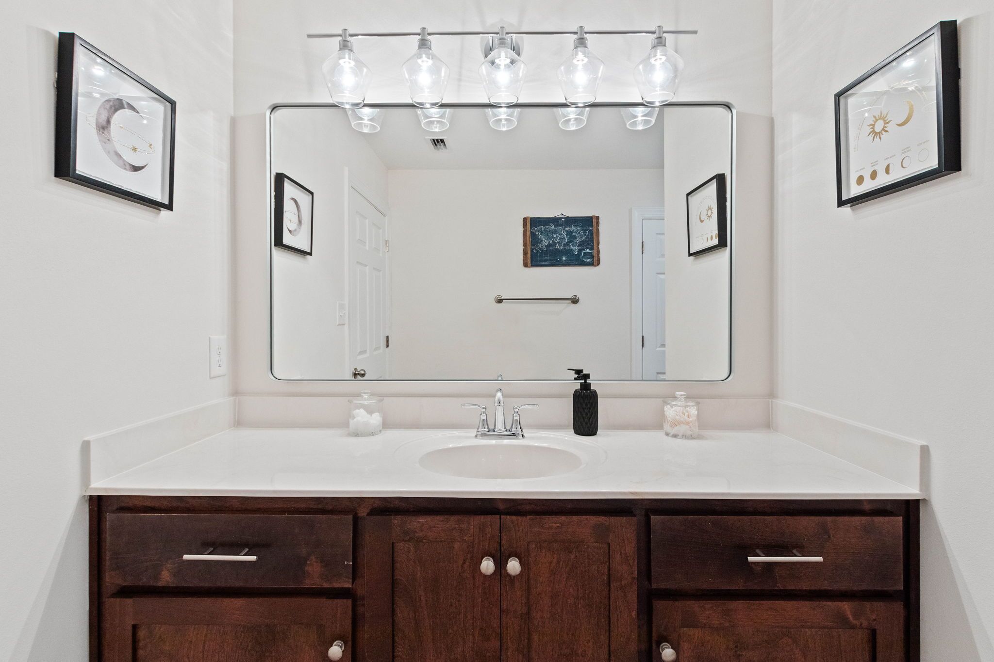 Un baño con un espejo grande, un lavamanos blanco y armarios de madera oscura.