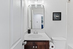 A bathroom with a white sink, a mirror, a toilet, and a framed picture on the wall.
