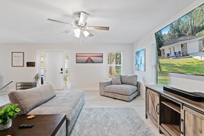 Ein modernes Wohnzimmer mit einem grauen Sofa, einem Sessel und einem Flachbildfernseher auf einer Holzkommode.