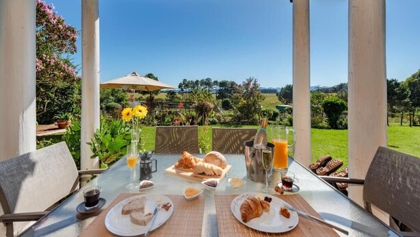 Ein Essbereich im Freien mit einem für das Frühstück gedeckten Tisch, Blick auf die Landschaft und einer Pergola.