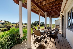 Um pátio externo com deck de madeira, pilares brancos e uma mesa posta para refeições.