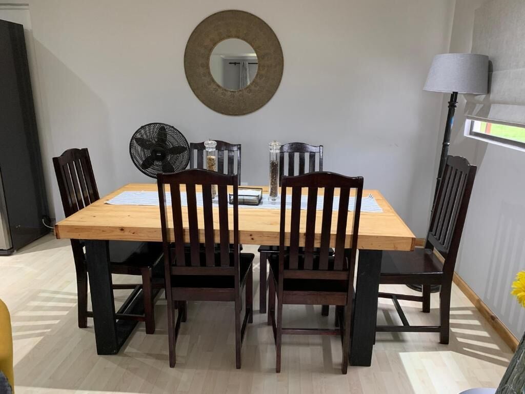Un coin repas avec une table et des chaises en bois, un miroir fixé au mur et une lampe sur pied.