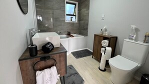 Ein modernes Badezimmer mit einer Badewanne, einer Toilette, einem Waschbecken und einem Schminktisch mit Handtuchhalter.
