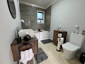 Um banheiro moderno com banheira, vaso sanitário, pia e toucador com porta-toalhas.