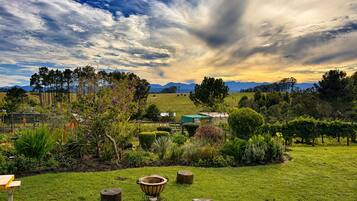 A grassy outdoor area with a wooden table and benches, surrounded by trees and a view of distant mountains.