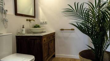 A bathroom with a toilet, a sink with a bowl, a mirror, a plant, and a wooden cabinet.