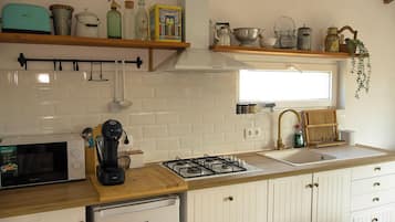 A kitchen with white cabinetry, a gas stove, a microwave, and various kitchen utensils on shelves.